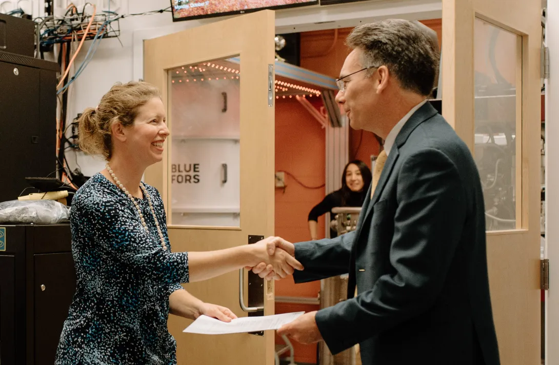 Two people shake hands while holding contracts